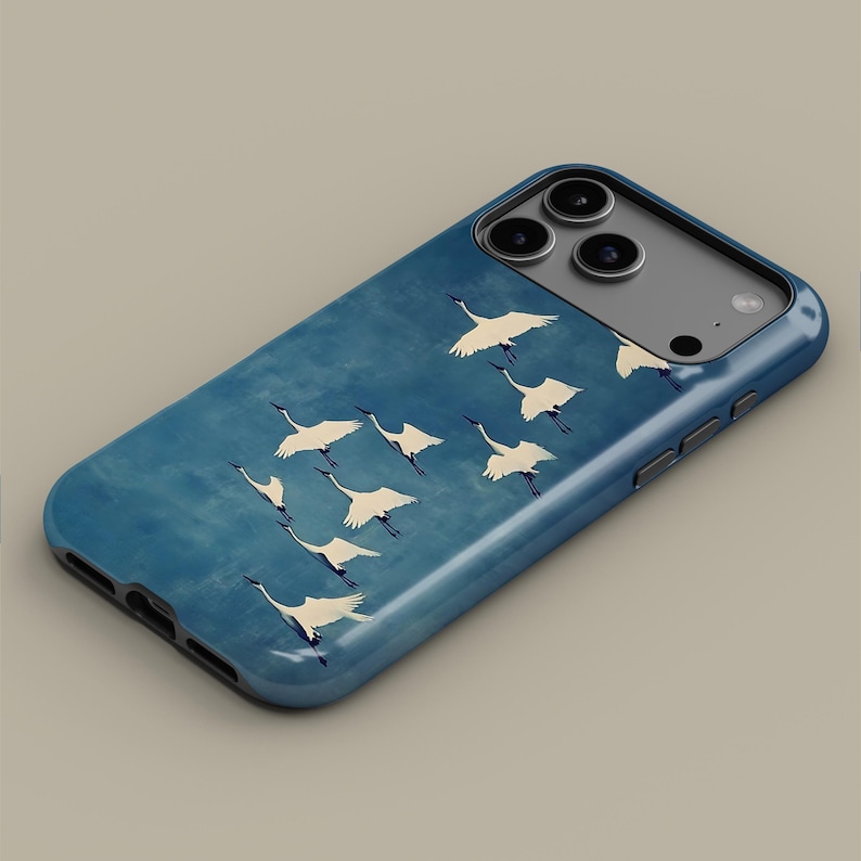 May include: A blue phone case featuring a flock of white cranes in flight against a textured blue background. The case has a glossy finish and a dark blue border, designed to fit a smartphone. The design evokes a sense of nature and tranquility.