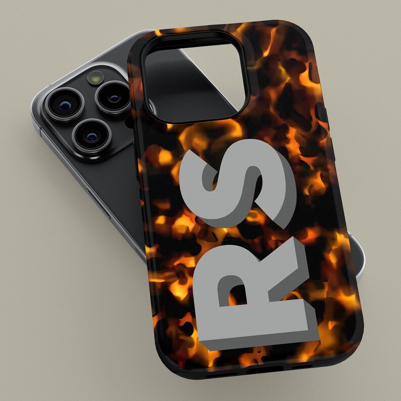 Puede incluir: Una funda de tel&eacute;fono negra con un patr&oacute;n de caparaz&oacute;n de tortuga y las letras "RS" en una fuente 3D gris.