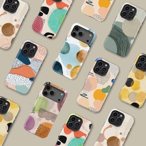 May include: A selection of phone cases with abstract designs. The cases display colourful patterns with shapes, dots, and lines in shades of blue, orange, green, and yellow. The cases are arranged on a neutral background.