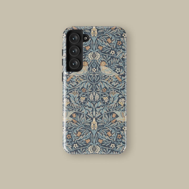 May include: A phone case with a navy blue floral pattern featuring birds, leaves, and flowers in shades of blue, beige, and orange. The case has a glossy finish and a camera module with three lenses.