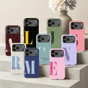 Könnte beinhalten: Eine Sammlung von neun Smartphone-Hüllen in verschiedenen Unifarben wie Bordeaux, Schwarz, Olivgrün, Hellblau, Marineblau, Pink und Lavendel. Jede Hülle ist mit einem großen, fetten Anfangsbuchstaben in Serifenschrift und einem Namen in Schreibschrift bedruckt.