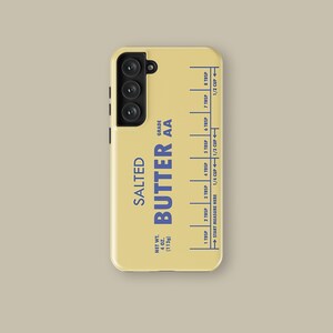 May include: A yellow phone case with a butter stick label design. The label reads "SALTED BUTTER AA" and includes a measurement guide in tablespoons and cups. The case has a black camera housing with three lenses.