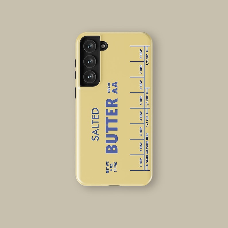 May include: A yellow phone case with a butter stick label design. The label reads "SALTED BUTTER AA" and includes a measurement guide in tablespoons and cups. The case has a black camera housing with three lenses.