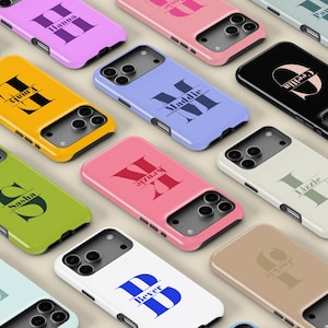 May include: A collection of personalized phone cases in various colors, each featuring a name and initial design. The cases are in shades of pink, yellow, green, blue, and black, with names like "Hanna," "Emily," and "Sasha" displayed.