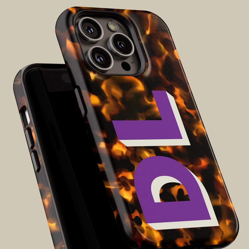 Puede incluir: Una funda para iPhone de caparaz&oacute;n de tortuga con un monograma "DL" morado y blanco impreso en la parte posterior.
