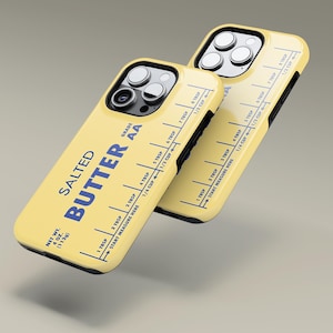 May include: A yellow iPhone case with a butter stick label design. The label reads "Salted Butter Grade AA" and has a measurement guide in tablespoons and cups. The case is designed to look like a vintage butter stick.
