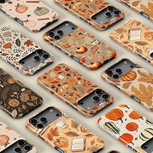 May include: A selection of phone cases with autumnal patterns. The cases display pumpkins, leaves, coffee cups, and books in orange, brown, and beige hues. The cases are arranged in a grid, highlighting the range of designs available.
