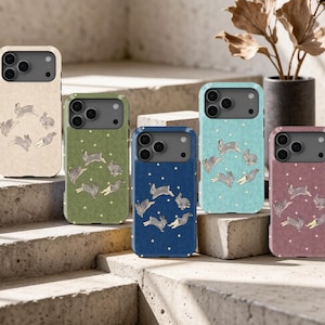 May include: Five smartphone cases in beige, olive green, navy blue, light blue, and dusty rose, each featuring a repeating pattern of small grey rabbits in various jumping poses interspersed with tiny white stars across the back surface.