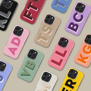 May include: A collection of colorful phone cases, each displaying a unique two-letter or three-letter initial design. The cases come in various colors, including pink, green, yellow, and black, with the letters in contrasting colors.