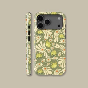 May include: A green phone case featuring a repeating pattern of white daisies and cartoon frogs. The case has a matte finish and a protective design, with cutouts for the camera and buttons. The side of the case also displays the daisy and frog pattern.