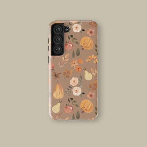 May include: A phone case with a brown background and a repeating pattern of pumpkins, pears, flowers, and leaves in shades of orange, peach, and cream. The case has a camera module with three lenses and a flash.