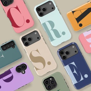 Może przedstawiać: Kolekcja kolorowych etui na telefony, każde z inną literą alfabetu. Etui są w różnych kolorach, w tym różowym, niebieskim, beżowym i zielonym. Litery są w pogrubionej, stylizowanej czcionce, z pasującą kropką. Etui są ułożone w atrakcyjny wzór.