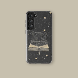 Op de afbeelding: Zwarte telefoonhoes met een slapende zwarte kat op een open boek. De achtergrond is een donkere sterrenhemel met gouden sterren. De hoes heeft een camera en volumeknoppen aan de zijkant.
