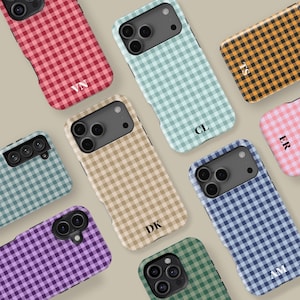 Puede incluir: Una colección de fundas para teléfonos con un patrón de cuadros vichy en varios colores, como rojo, azul, verde y beige. Cada funda tiene una inicial diferente impresa. Las fundas están diseñadas para diferentes modelos de teléfonos.