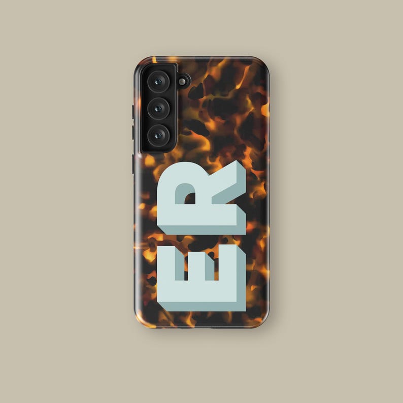Puede incluir: Una funda de tel&eacute;fono con un patr&oacute;n de caparaz&oacute;n de tortuga y las letras "ER" en blanco en la parte posterior.