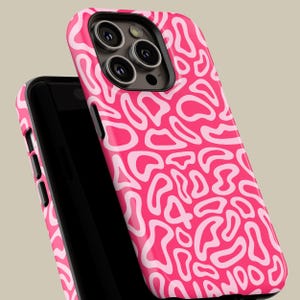 May include: A hot pink phone case with a white abstract pattern. The case is shown on a black phone, with the camera lenses visible. The design features a repeating, organic shape.
