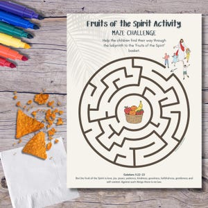May include: A printed activity sheet titled "Fruits of the Spirit Activity MAZE CHALLENGE" features a brown maze with a basket of fruit at the center. The sheet includes text and illustrations, with colorful markers and snacks on a wooden surface.