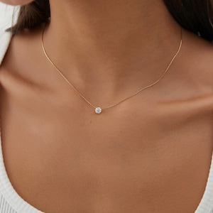Può includere: Una delicata collana a catena d'oro con un unico ciondolo rotondo in pietra preziosa trasparente.