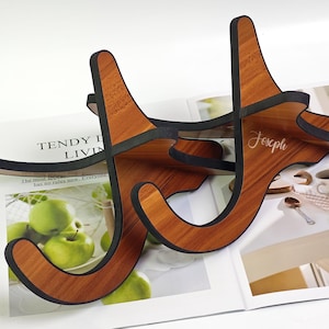 May include: Two wooden guitar stands with black edging. The stand on the right has the name "Joseph" engraved on it.