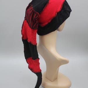 Puede incluir: Un sombrero de patchwork caprichoso con una larga cola puntiaguda. El sombrero presenta secciones alternas de tela roja y negra, incluidos patrones acanalados y a rayas. El sombrero se exhibe en una cabeza de maniquí.