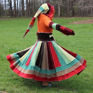 May include: A colorful, multi-layered dress with a long, flowing skirt. The dress is made from different types of fabric, including knit and velvet. The dress has a hood and a long, flowing train.