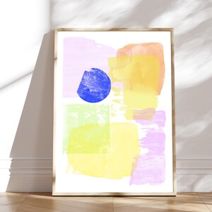 Könnte beinhalten: Abstrakter Kunstdruck mit einem blauen Kreis, gelben, grünen, rosa und orangefarbenen Aquarellformen. Der Druck ist in einem hellen Holzrahmen gerahmt.