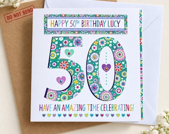 May include: A square white birthday card featuring the text HAPPY 50TH BIRTHDAY LUCY and HAVE AN AMAZING TIME CELEBRATING. The number 50 is large, teal, and decorated with a colorful floral pattern, small hearts, and embedded crystals.