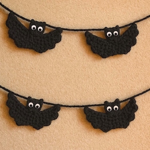 Puede incluir: Guirnalda de Halloween de ganchillo negro con cuatro murciélagos. Cada murciélago tiene ojos blancos y está ensartado en un cordón negro. Los murciélagos están espaciados uniformemente y cuelgan sobre un fondo beige.
