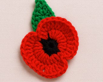 May include: A handcrafted crochet poppy flower applique featuring vibrant red petals, a solid black center, and a single green leaf extending from the top. The textured yarn construction creates a layered, circular floral design with visible stitches.