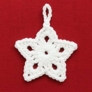 May include: A white, crocheted star ornament with a loop for hanging. The star has five points and openwork details. The background is a solid red.