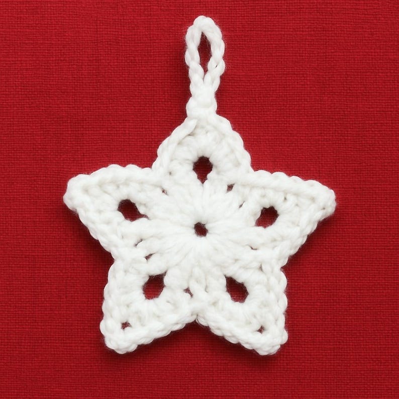 May include: A white, crocheted star ornament with a loop for hanging. The star has five points and openwork details. The background is a solid red.
