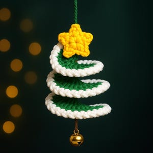 May include: A handmade crochet Christmas tree ornament. The tree is green with white trim and a yellow star on top. A small gold bell hangs from the bottom. The ornament is suspended by a green string against a dark green background.
