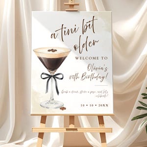 May include: A sign on an easel with the text "a tini bit older" and "Welcome to Olivia's 30th Birthday!" A watercolor illustration of a cocktail with coffee beans and a black bow is featured. The sign also includes the date 10.10.20XX.
