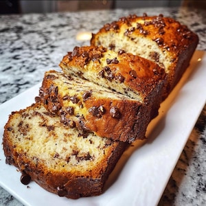 Könnte beinhalten: Geschnittenes Bananenbrot mit Schokoladenstückchen auf einem weißen rechteckigen Teller. Das Brot hat eine goldbraune Kruste und ist mit Schokoladenstückchen übersät. Die Scheiben zeigen ein feuchtes Inneres.