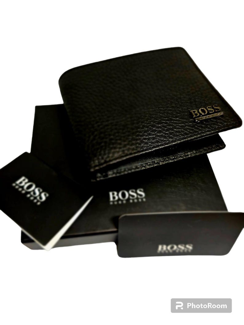 May include: Black leather wallet with the BOSS logo embossed on the front. The wallet is displayed with its original packaging, including a box and a card, all bearing the BOSS brand name. The wallet has a textured surface.