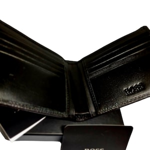 May include: Open black leather wallet with multiple card slots and a bill compartment. The wallet is displayed open, revealing its interior. A black card with the "BOSS" logo is in front of the wallet.