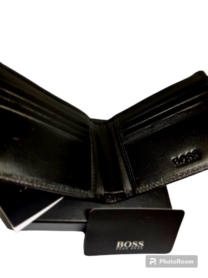 May include: Open black leather wallet with multiple card slots and a bill compartment. The wallet is displayed open, revealing its interior. A black card with the "BOSS" logo is in front of the wallet.