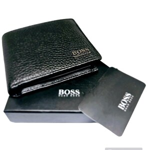 May include: Black leather wallet with a textured finish. The wallet has the word "BOSS" in silver lettering on the front. A black card and a black box with the word "BOSS" are also visible.