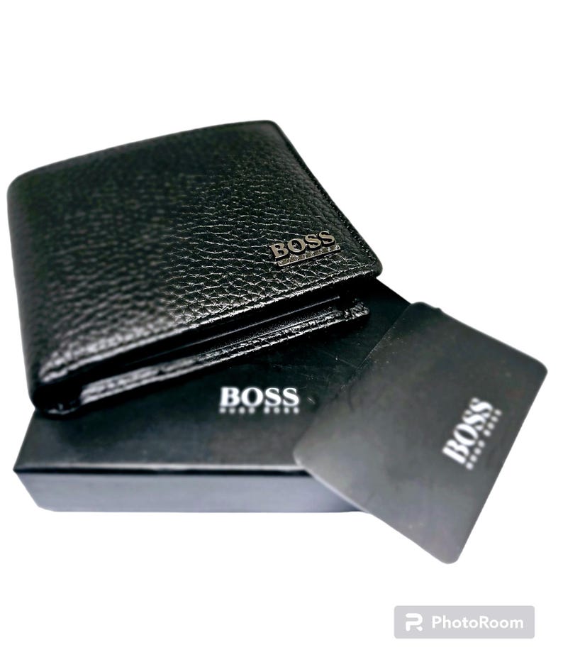May include: Black leather wallet with a textured finish. The wallet has the word "BOSS" in silver lettering on the front. A black card and a black box with the word "BOSS" are also visible.