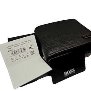 May include: A dark brown leather wallet with a textured surface. The wallet has the brand name "BOSS" embossed on the front. A white tag with the text "Monist" and a barcode is visible.