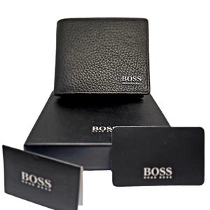 Może przedstawiać: Czarny skórzany portfel z nazwą marki "BOSS" w srebrnych literach. Portfel jest prezentowany na czarnym pudełku i w towarzystwie dwóch czarnych kart, również z logo "BOSS". Portfel ma teksturowaną powierzchnię.