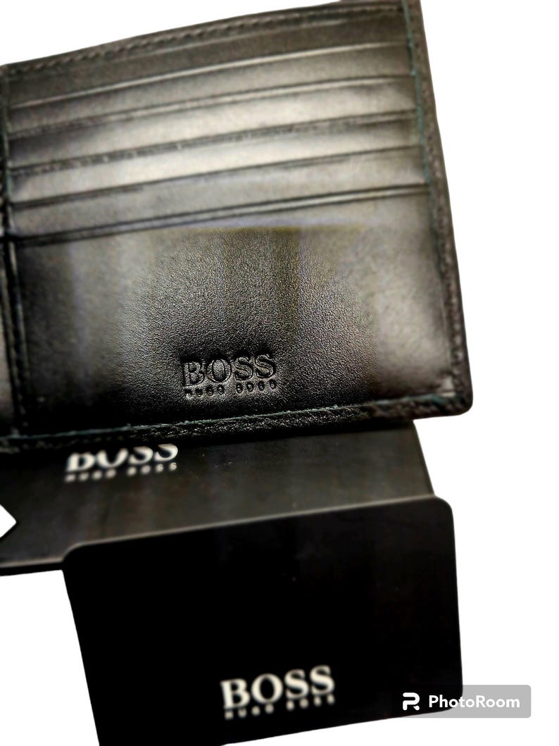 May include: Black leather wallet with the embossed brand name "BOSS". The wallet is open, revealing multiple card slots. A black card with the brand name "BOSS" is visible below the wallet.