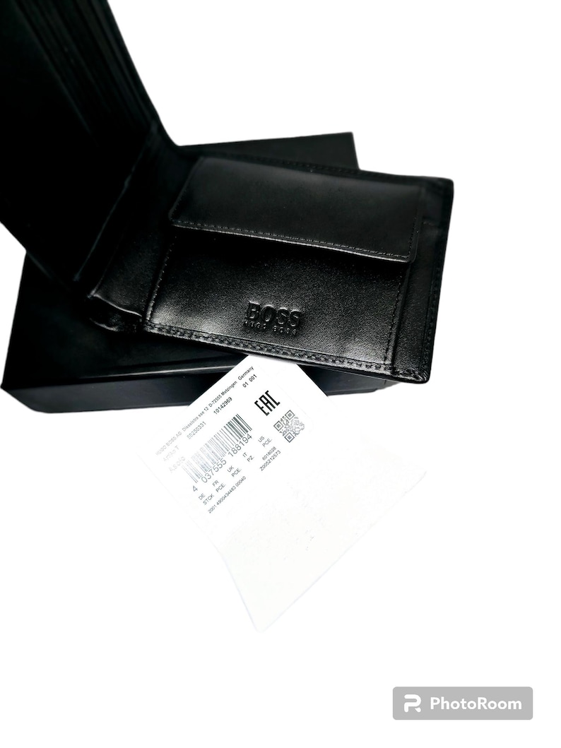 Pode incluir: Carteira de couro preta com o nome da marca "BOSS" em relevo na frente. A carteira est&aacute; aberta, revelando os compartimentos internos. Um pequeno bolso quadrado para moedas &eacute; vis&iacute;vel. Uma etiqueta branca com texto e um c&oacute;digo de barras est&aacute; em primeiro plano.