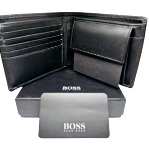 May include: Open black leather wallet with multiple card slots and a coin pocket. The wallet is displayed open on top of a black box and a card, both with the brand name "BOSS" printed in white.