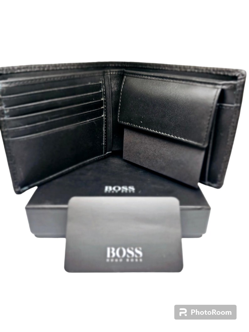 May include: Open black leather wallet with multiple card slots and a coin pocket. The wallet is displayed open on top of a black box and a card, both with the brand name "BOSS" printed in white.
