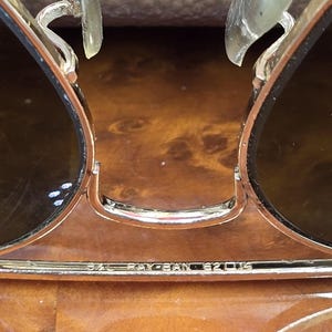 May include: Close-up of gold-framed sunglasses with dark lenses. The Ray-Ban logo is visible on the frame. The sunglasses have clear nose pads and a classic aviator design.