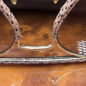 May include: Close-up of vintage sunglasses with gold frames and brown lenses. The temples are covered in a spotted, light brown material. The text "BAL 58 14 USA" is visible on the frame.