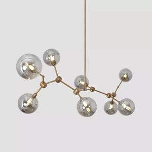 May include: A contemporary chandelier with multiple spherical glass shades with a mirrored finish. The shades are attached to a brass-coloured metal frame, creating a unique lighting fixture. The light bulbs are visible inside the glass spheres.