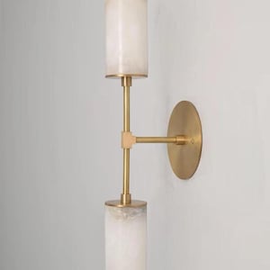 Può includere: Applique da parete moderna con due paralumi cilindrici bianco sporco e finitura in ottone. L'applique è montata su una piastra circolare in ottone, con i paralumi collegati da un braccio in ottone. Gli apparecchi sono cilindrici.