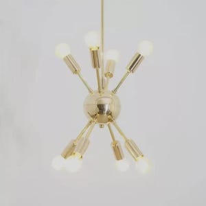 May include: A gold-coloured, sputnik-style chandelier with multiple arms extending from a central sphere. Each arm holds a light bulb, creating a starburst effect. The fixture is suspended from a single point.